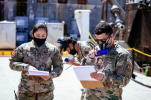 Three airmen are working on liquid rocket CONOPS and novel deployable systems tests by referencing their clipboards and speaking into walkie-talkies.