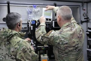 Maj. Thomas Heering and Maj. Adam Faltersack stand before the tactical anesthesia workstation (TAW) while setting it up for a Ground Surgical Team (GST) training course.