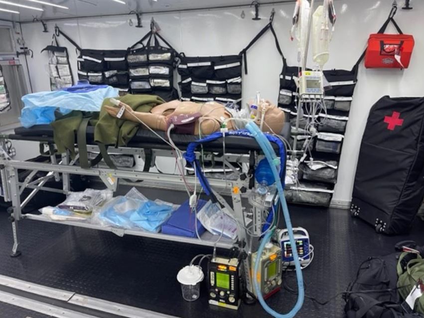 A field-type operating room within the Ground Surgical Team (GST) including a manikin laying on a gurney and attached to medical equipment.