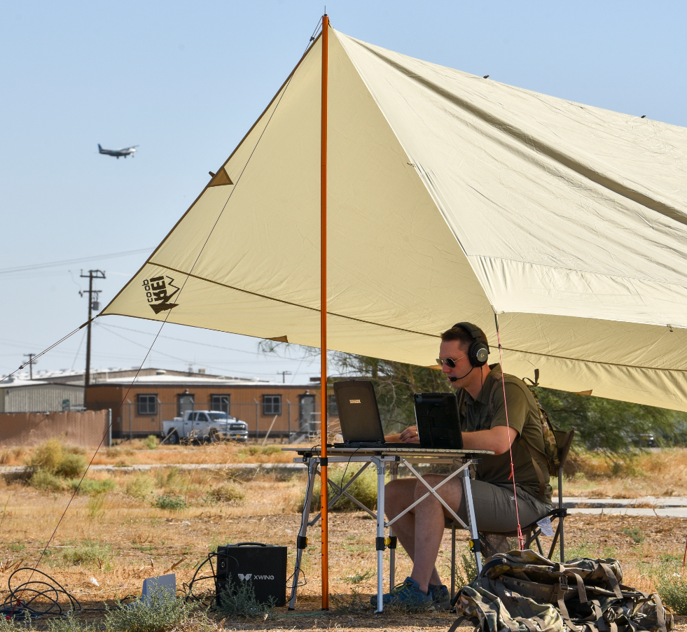 Team member sits monitoring a laptop under a propped up tent area.