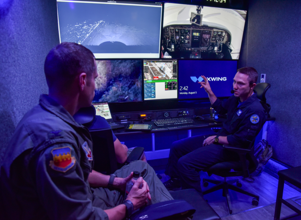 Two Airmen sit in a blue tinted operations room looking at monitors covering the flight test.