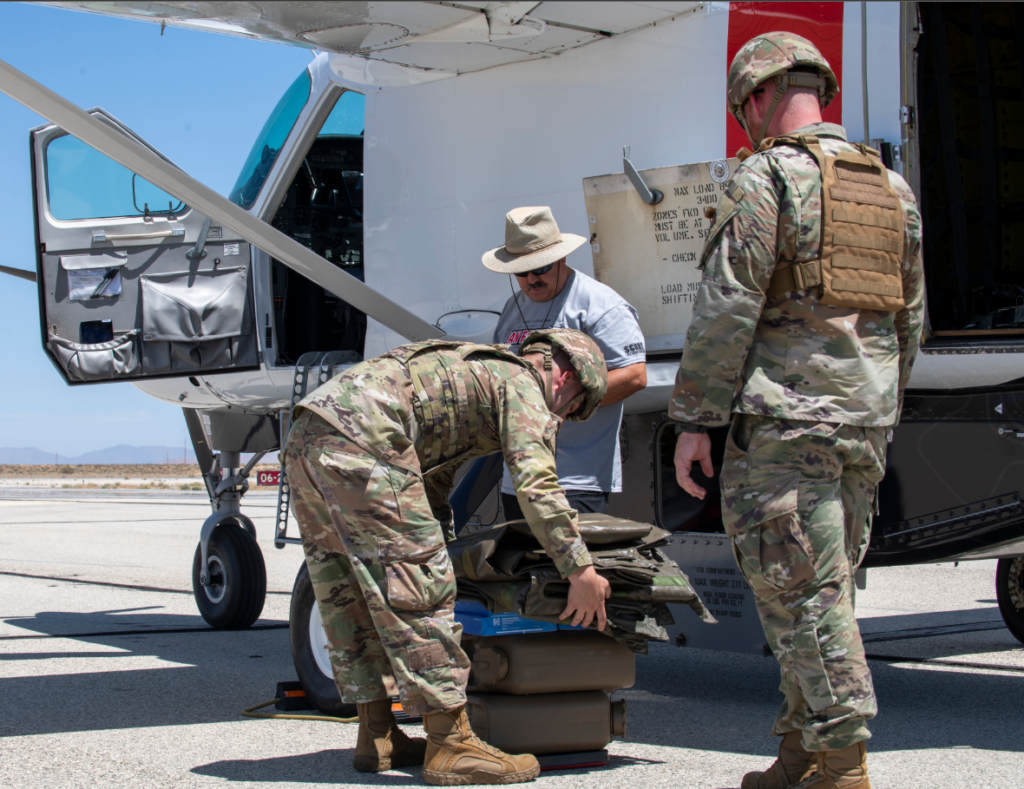 Two Airmen in fatigues load up test craft alongside a plain clothes team member.